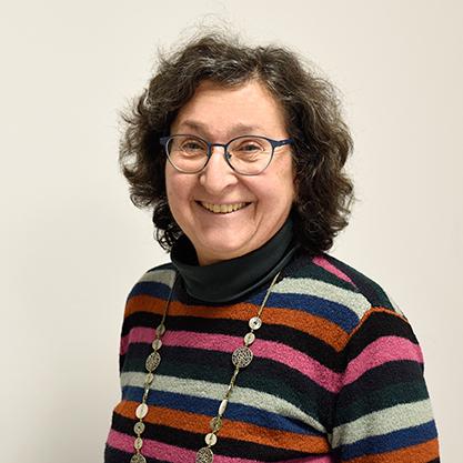 Lächelnde Frau mit lockigem, braunem Haar, trägt ein gestreiftes Oberteil und eine Kette, vor neutralem Hintergrund.