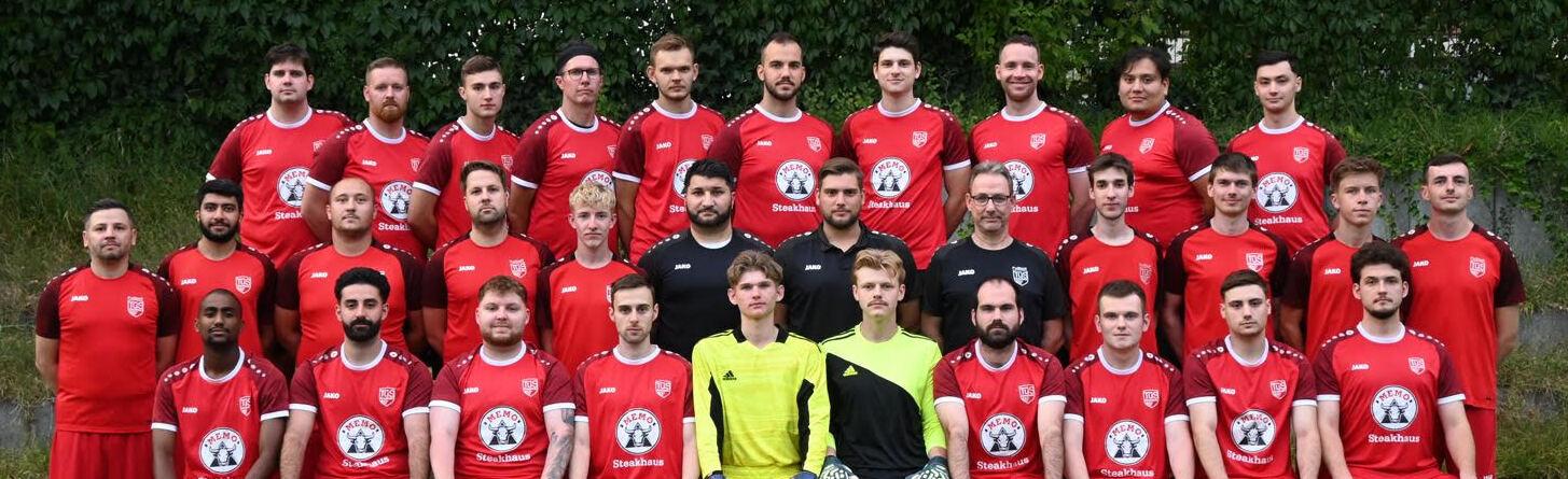 Mannschaftsbild von einem Fu&szlig;ballteam in roten Trikots, auf einem gr&uuml;nen Rasen, mit 36 Spielern und einem Trainer.