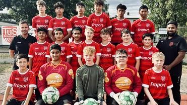 Gruppenfoto einer Jugendfußballmannschaft in roten Trikots, ergänzt durch Trainer und Torwarte mit Bällen in der Hand.