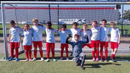 Gruppe von zehn Kindern im Fußballtrikot vor einem Tor auf einem Rasenplatz, strahlend und lächelnd für das Foto.