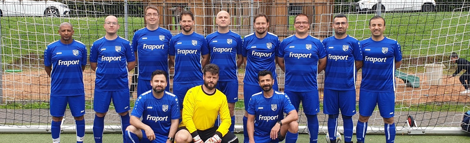 Mannschaftsfoto einer Fu&szlig;ballmannschaft in blauen Trikots vor einem Tor auf einem Kunstrasenplatz.
