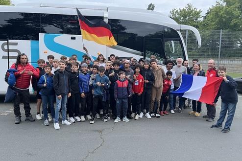 Gruppe von jungen Sportlern mit zwei Trainern, die vor einem Reisebus stehen und eine französische Flagge halten.
