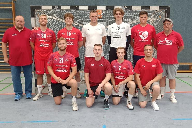 Mannschaftsbild einer Handballmannschaft in roter und schwarzer Sportkleidung vor einem Handballtor.