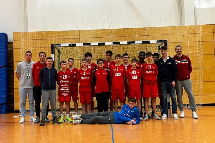 Gruppe von Handballspielern in roten Trikots posiert vor einem Tor in einer Sporthalle.