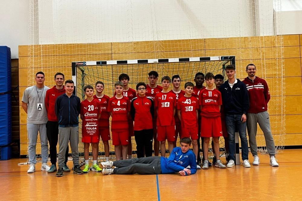 Gruppe von Handballspielern in roten Trikots posiert vor einem Tor in einer Sporthalle.