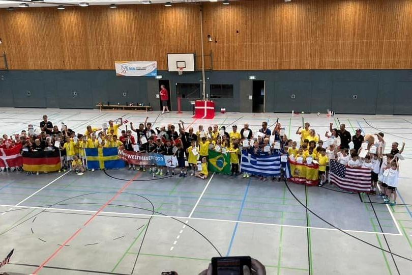 Gruppenfoto von Kindern in Sportkleidung mitflaggen verschiedener Länder in einer Sporthalle.