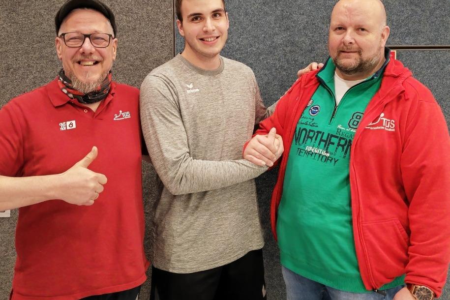 Drei Männer stehen in einer Sporthalle, einer schüttelt die Hand des anderen, während der Dritte Daumen hoch zeigt.