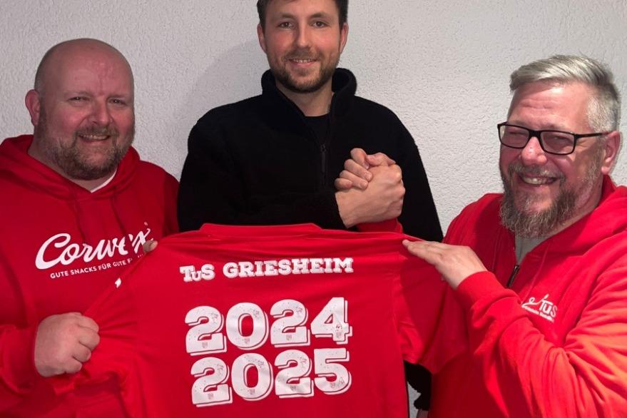 Drei Männer in roten Sweatshirts halten ein T-Shirt mit der Aufschrift „TuS Griesheim 2024 2025 Welcome REWE Michael Weisbrod“.