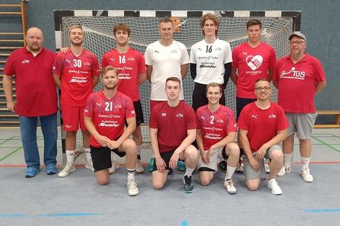 Mannschaftsbild einer Handballmannschaft in roter und schwarzer Sportkleidung vor einem Handballtor.