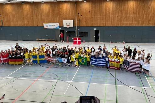 Gruppenfoto von Kindern in Sportkleidung mitflaggen verschiedener Länder in einer Sporthalle.
