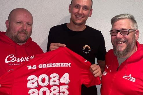 Drei Männer präsentieren ein rotes Trikot mit der Aufschrift "TuS Griesheim 2024-2025 Welcome REWE" vor einer hellen Wand.