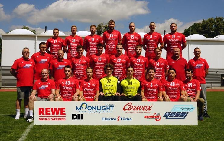 Mannschaftsfoto einer Fußballmannschaft in roten Trikots, stehend und sitzend vor einem Werbebanner im Freien.