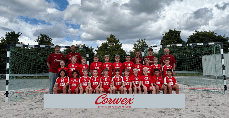 Gruppenfoto einer Jugendfußballmannschaft in roten Trikots vor einem Tor auf einem Sandplatz.