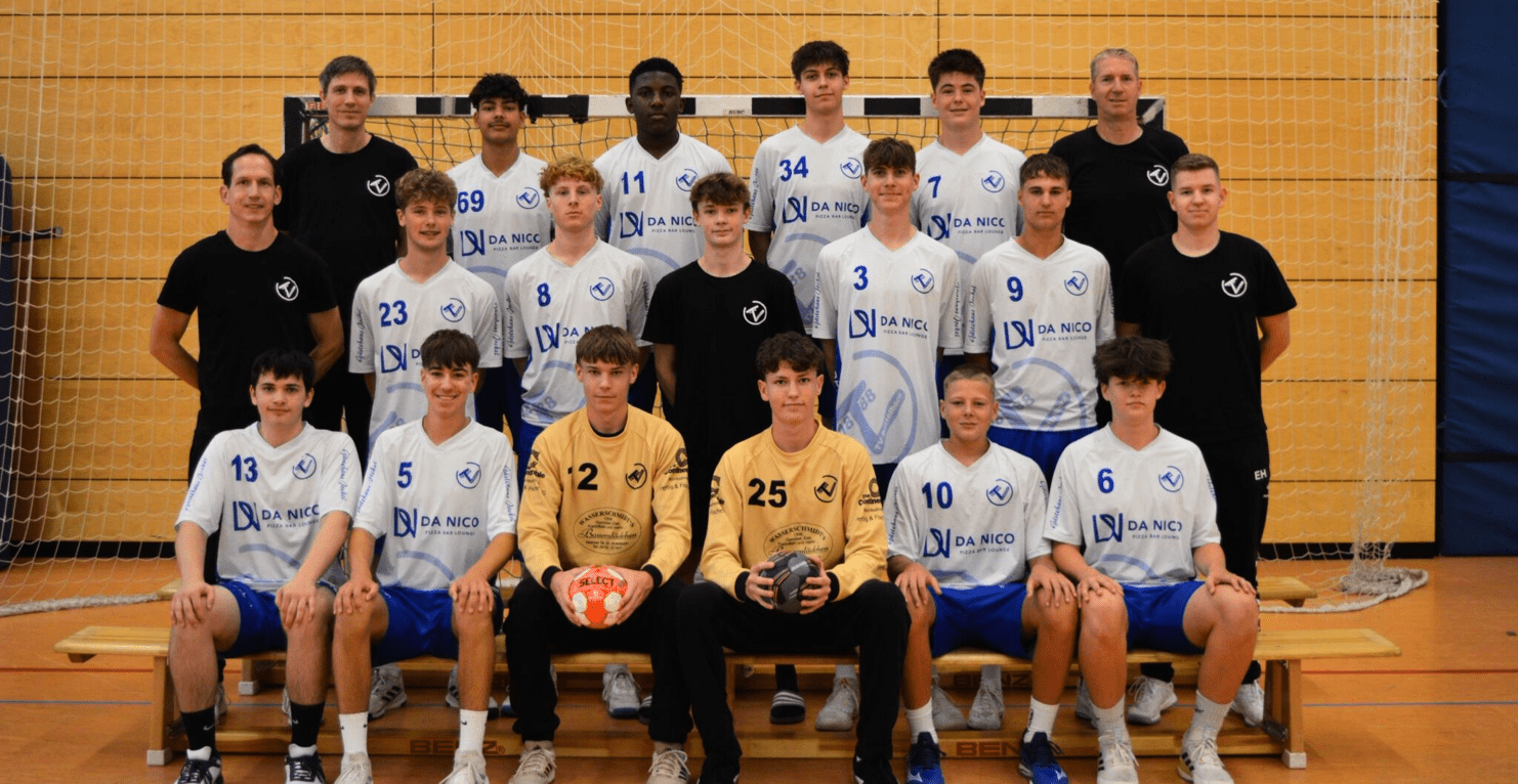 Gruppenbild einer Handballmannschaft mit Trainern, in einheitlichen Trikots und Shorts, vor einem Handballtor.