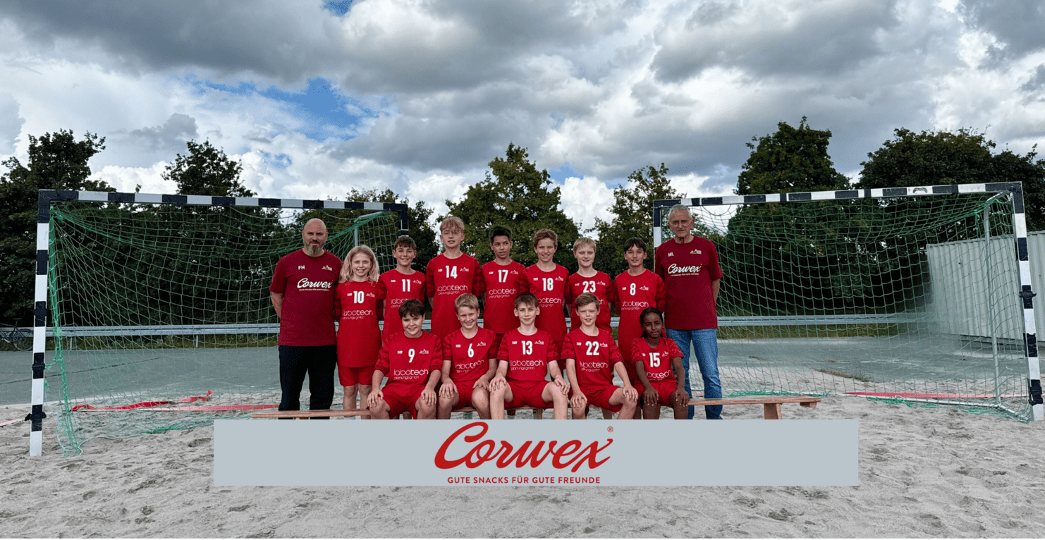 Gruppenfoto einer Fußballmannschaft mit 12 Spielern und 2 Trainern auf einem Sandplatz vor einem Tor.