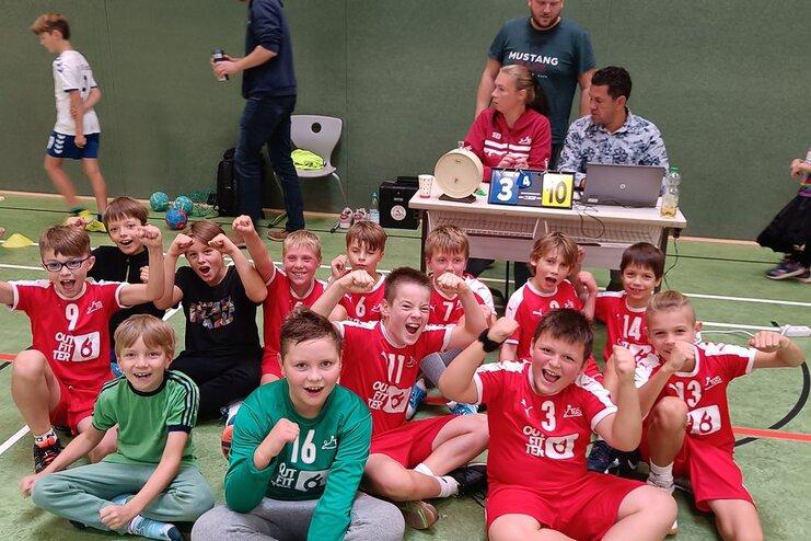 Gruppe von Kindern in Sportkleidung posiert fröhlich auf dem Boden einer Sporthalle nach einem Handballspiel.