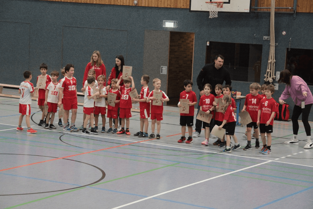 Gruppe von Kindern in roten Trikots steht in einer Sporthalle und hält Urkunden in den Händen.
