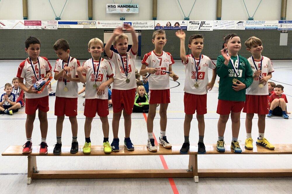 Gruppe von Jungen in Sportkleidung mit Medaillen stehen auf einer Bank, feiern ihre Erfolge in einer Sporthalle.