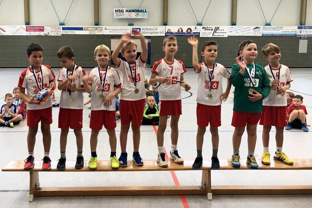 Gruppe von Jungen in Sportkleidung mit Medaillen stehen auf einer Bank, feiern ihre Erfolge in einer Sporthalle.