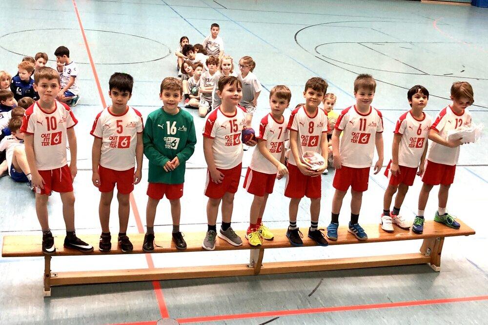 Acht Jungen in Sportkleidung stehen auf einer Bank in einer Sporthalle, im Hintergrund sitzen weitere Kinder.