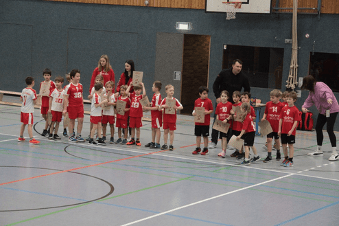 Gruppe von Kindern in roten Trikots steht in einer Sporthalle und hält Urkunden in den Händen.