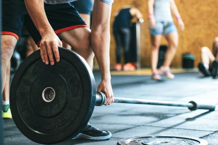 Nahaufnahme eines Sportlers, der eine Gewichtsscheibe an einer Langhantel im Fitnessstudio hebt.