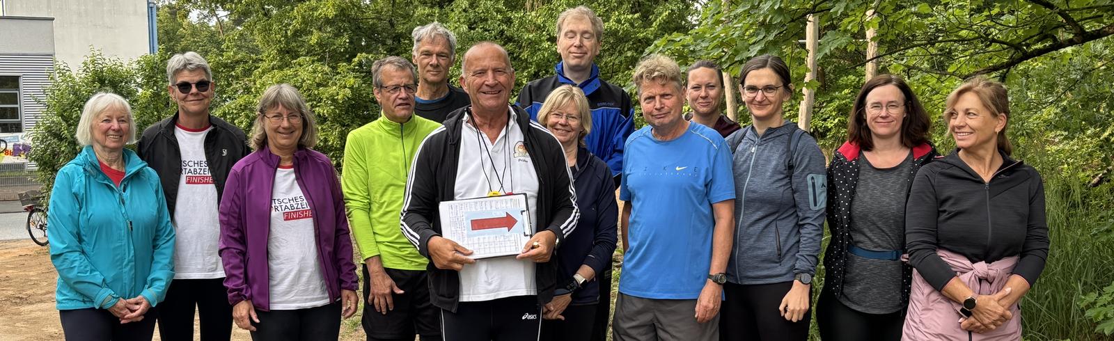 Gruppe von L&auml;ufern in Sportkleidung posiert im Freien, einige halten ein Zertifikat in der Hand.