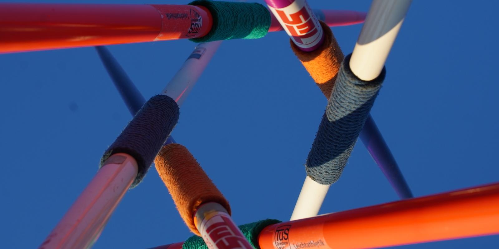 Draufsicht auf miteinander verbundene Stangen mit bunten Knoten, vor klarem blauen Himmel.