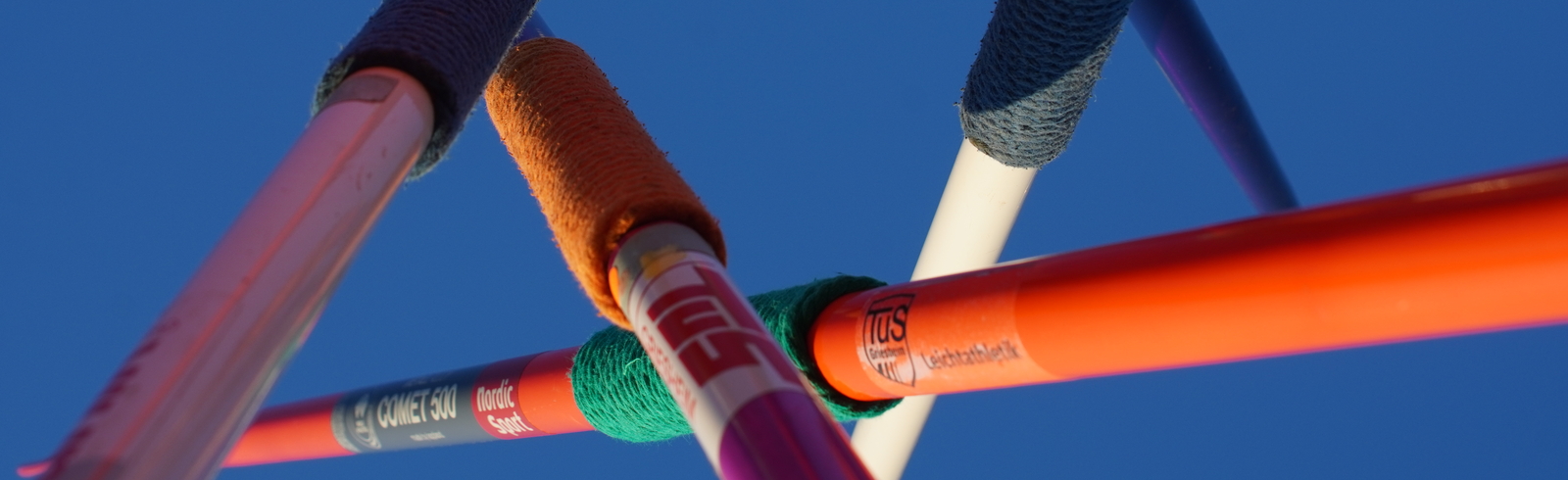 Draufsicht auf miteinander verbundene Stangen mit bunten Knoten, vor klarem blauen Himmel.