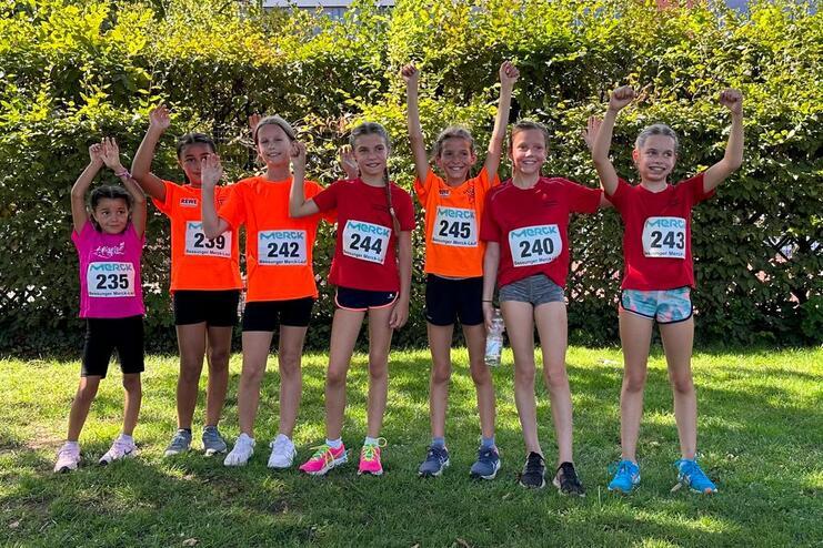 Gruppe von sechs M&auml;dchen in Sportbekleidung mit Teilnehmernummern, die fr&ouml;hlich im Freien posieren.