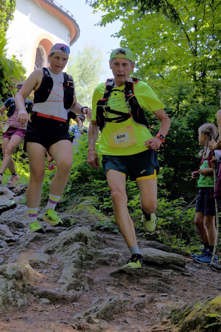 Zwei Läuferinnen steigen über einen steinigen Weg, umgeben von Bäumen und Zuschauern, bei einem Trailrun-Event.