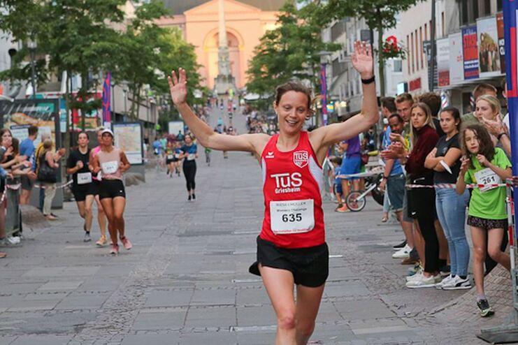 L&auml;uferin in rotem Trikot mit Armen in der Luft beim Zieleinlauf einer Stra&szlig;ensportveranstaltung, Zuschauer applaudieren.