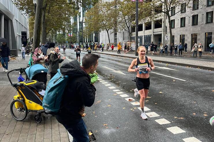 L&auml;uferin bei einem Wettkampf in einer Stadtstra&szlig;e, umgeben von Zuschauern und herbstlichen B&auml;umen.