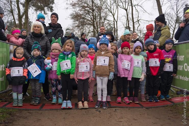 Kinder in Sportkleidung warten am Start einer Laufveranstaltung, umringt von Zuschauern und Begleitern.