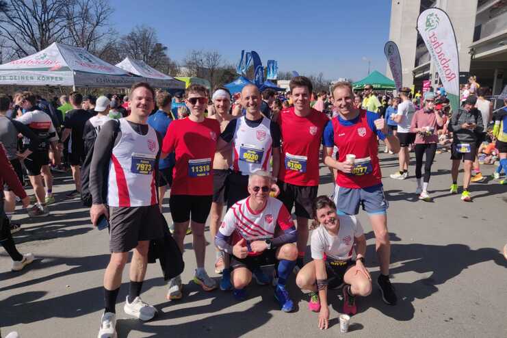 Gruppe von L&auml;ufern in Sportbekleidung posiert l&auml;chelnd vor einem Wettkampf bei sonnigem Wetter.