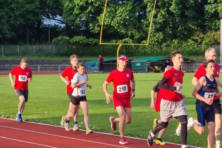 Gruppe von Läufern in roten Trikots auf einer Leichtathletikbahn in einem Wettkampf.