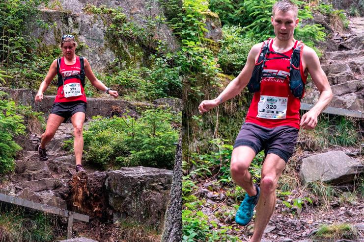 Zwei Trailrunner springen &uuml;ber unebenen Gel&auml;nde, umgeben von dichter gr&uuml;ner Vegetation und Felsen.