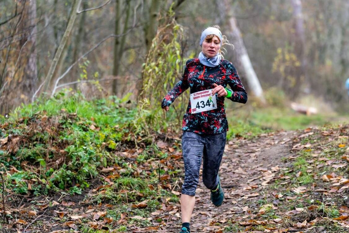 Läuferin in farbenfroher Sportkleidung überquert einen woodland Trail bei einem Wettkampf im Herbst.