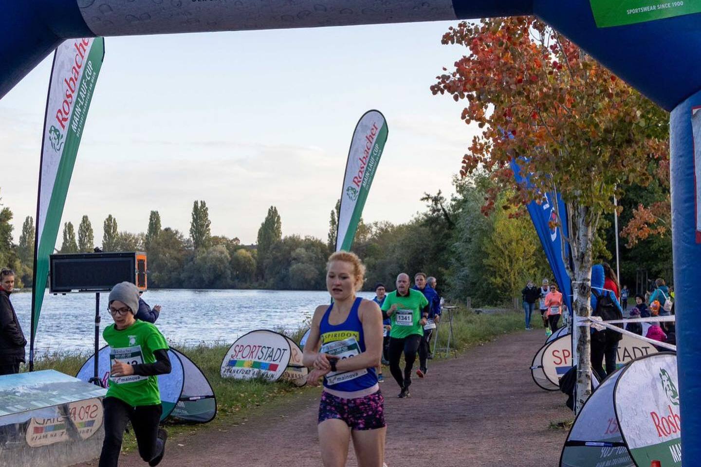 Läuferinnen und Läufer überqueren den Zielbogen beim Rosbacher Main-Lauf-Cup an einem Flussufer.