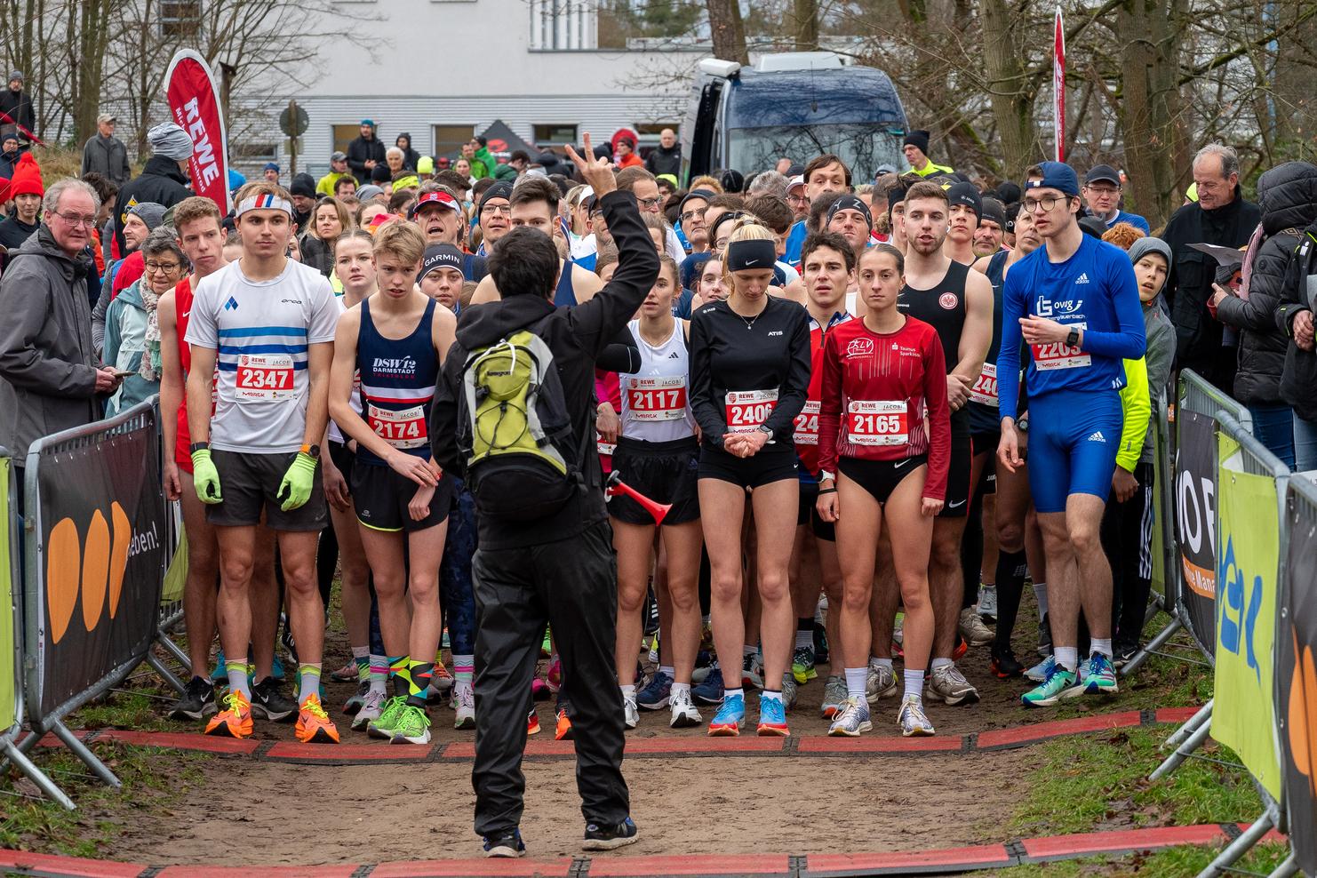 Startgruppe von Läufern beim Wettlauf, bereit zur Abfahrt, mit Zuschauerbereich im Hintergrund.