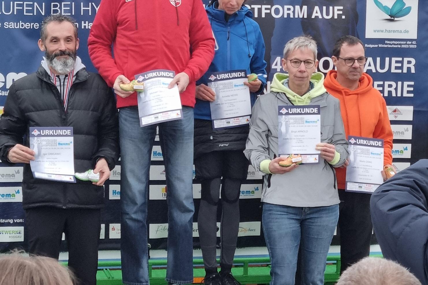 Siegerpodium mit fünf Personen, die Urkunden halten, bei einer Laufveranstaltung in outdoor Umgebung.