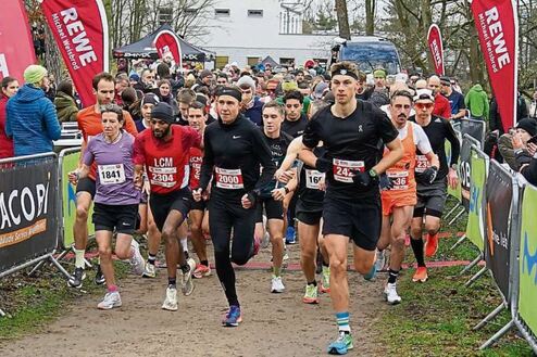 Start eines Wettlaufs mit mehreren Teilnehmern, umgeben von Zuschauern und Markierungen auf dem Boden.