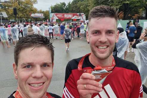Zwei Teilnehmer nach dem Münchner Marathon halten stolz ihre Medaillen in der Hand, umgeben von anderen Läufern.