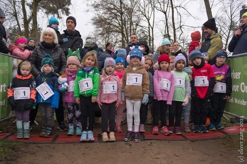 Kinder in Sportkleidung warten am Start einer Laufveranstaltung, umringt von Zuschauern und Begleitern.