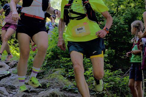 Zwei Läuferinnen steigen über einen steinigen Weg, umgeben von Bäumen und Zuschauern, bei einem Trailrun-Event.