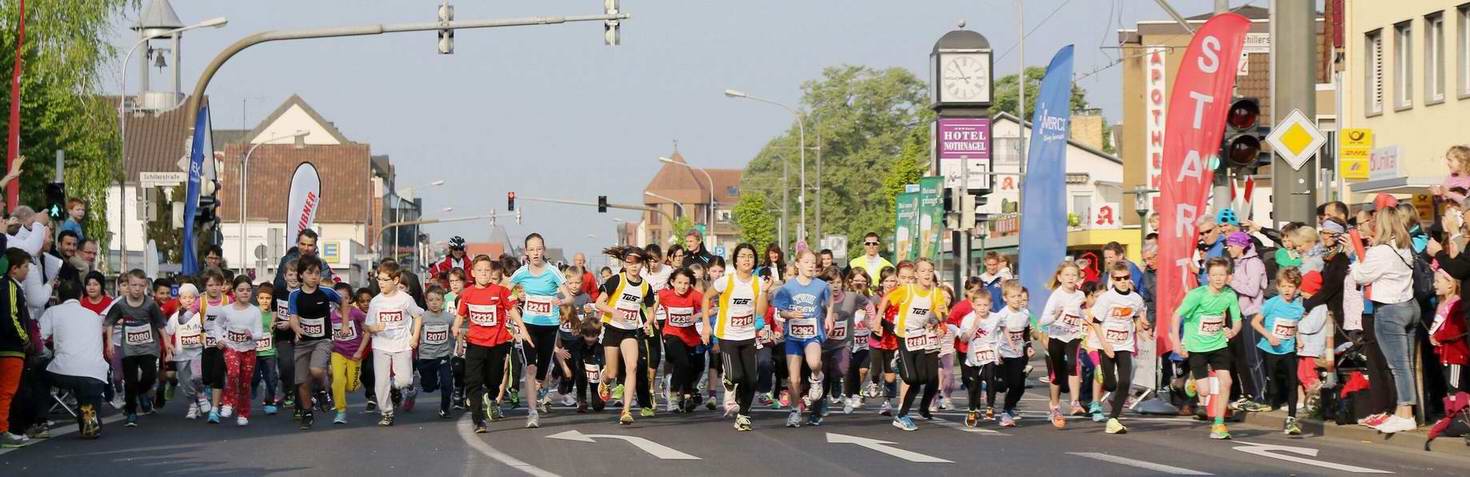 Startschuss für einen Kinderlauf: Zahlreiche laufende Kinder in Sportbekleidung auf einer Stadtstraße.