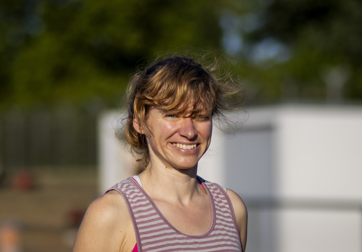 Lächelnde Frau mit ungekämmtem, lockigem Haar in einem gestreiften Oberteil vor unscharfem Hintergrund.