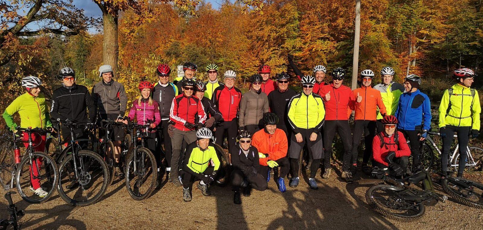 Gruppe von Radfahrern in bunter Kleidung posiert vor bunten Herbstb&auml;umen. Fahrr&auml;der stehen daneben.