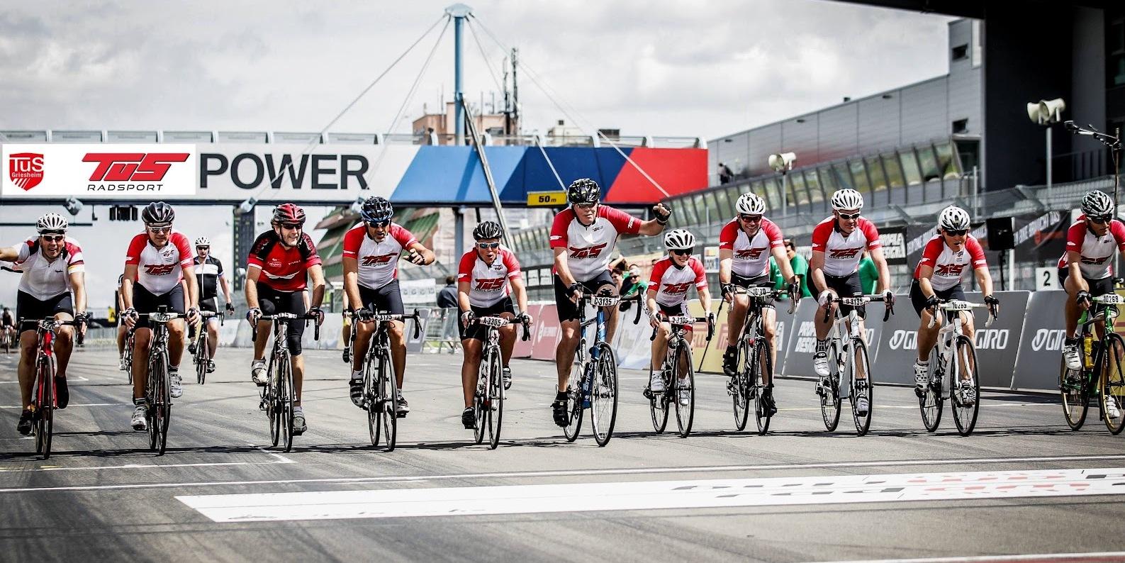 Gruppierung von Radfahrern in roten Shirts, die die Ziellinie auf einer Rennstrecke &uuml;berqueren.