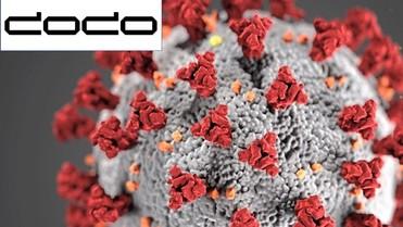 Detailreiche Mikroskopaufnahme eines Coronavirus mit roten Spitzen auf einer grauen Oberfläche.